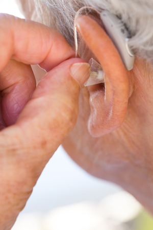 closeup senior woman inserting hearing aid in her earsの写真素材