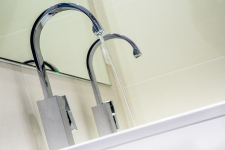 closeup on modern stainless steel faucet knob with flowing water