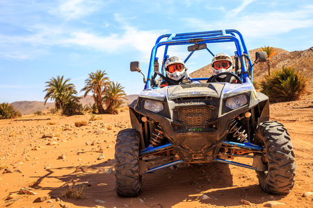 Merzouga, Morocco - Feb 26, 2016: front view on blue Polaris RZR 800 with it's pilots in Morocco desert near Merzouga. Merzouga is famous for its dunes, the highest in Morocco. There is a palm grove in the backgroundのeditorial素材