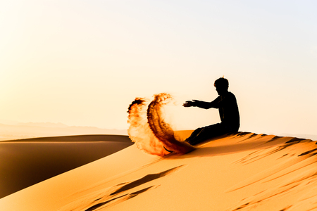 Silhouette of young man playing with sand on top of a dune of saharaの写真素材