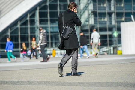 La defense, France- April 09, 2014: side view of businessman walking in a street by phoning. He wears shoulder strap bagのeditorial素材