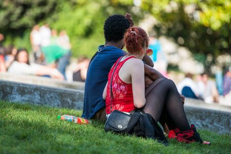 Paris, France- June 30, 2013: Young mixed race couple in love sitting in the grass in a park near the butte montmartreのeditorial素材