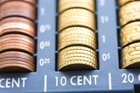 Open cash registrer containing many coins of euros in raw