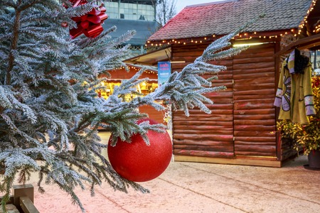 Niort, France - December 05, 2017:Close-up of a Christmas ball hanging on a snowy tree with Christmas market chalets in the backgroundのeditorial素材