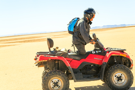 Merzouga, Morocco - February 22 2016: man going on a quad bike in the middle of the Moroccan desert on a sunny day, with mountains in the background.のeditorial素材