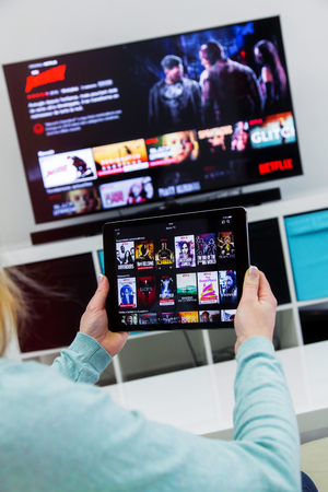 Benon, France - January 21, 2018: Woman Holding a touch pad and switching channels on France Netflix HomePage. with TV set on background. Netflix Inc. is an American multinational entertainment company founded on 1997のeditorial素材