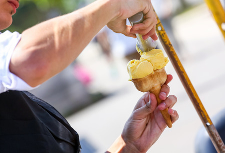 An ice-cream seller putting a scoop of ice-cream on a cone on a sunny dayの写真素材