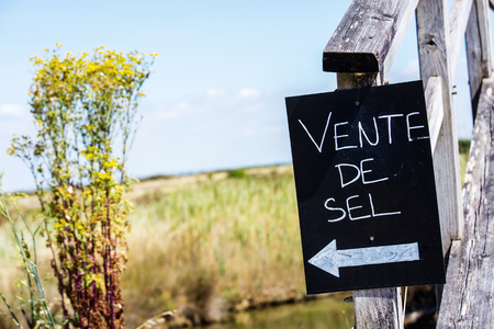 Closeup of sign - "Sale of Salt" ("Vente de Sel" in French) with field on backgroundの写真素材