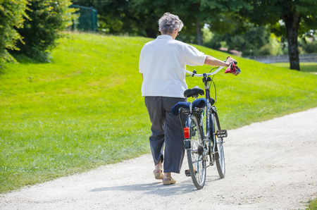 Surgeres, France - June 19, 2016 : Rear view of active senior woman walking with bike in park at Surgeres, Franceのeditorial素材