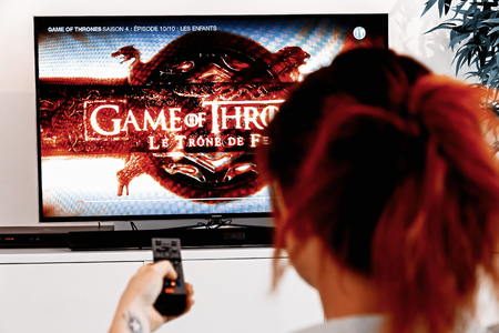 Benon, France - December 30, 2018: Woman Holding a TV remote and watch Game of thrones, an original creation of HBO industry. Created by David Benioff and D. B. Weiss, broadcast since 2011 on HBOのeditorial素材