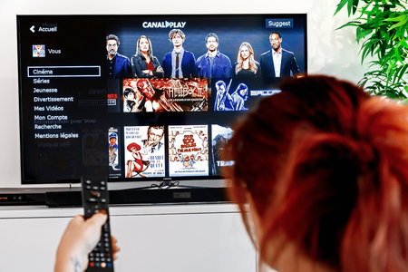 Benon, France - December 30, 2018: Woman holding a television remote control and watching homepage of canalplay. CanalPlay is a paid French Internet service for the distribution of video files.のeditorial素材