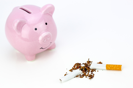 Cigarette cut in half and piggy bank. Stop smoking concept and save money. Concept of cost of tabacco, cigarettes.の写真素材