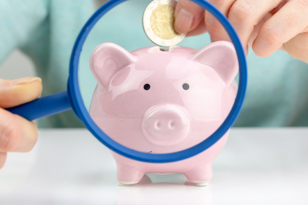 Woman Putting Coin In Piggy Bank. Zoom effect with a magnifying glassの写真素材