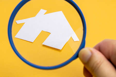 Paper house enlarged with a magnifying glass on a yellow background. Real estate conceptの写真素材