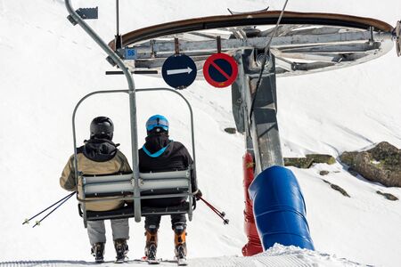 La Mongie, France - March 21, 2019:Back view of anonymous skiers riding chairlift over snowy mountain slope while resting on resort on sunny winter dayのeditorial素材