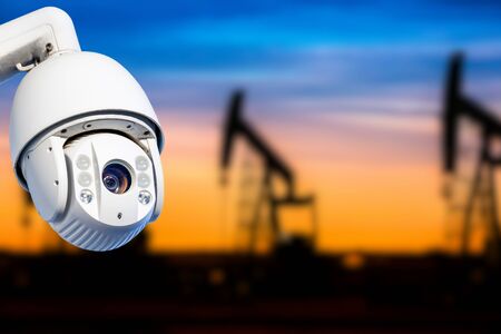 CCTV camera concept with silhouettes of oil well on oil field with nice sunset sky background