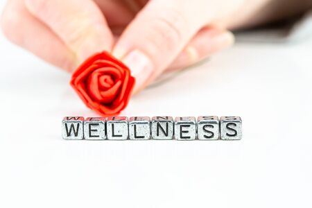 background wellness concept with cube letters and a woman hand holding a roseの写真素材