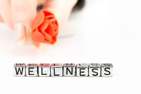 background wellness concept with cube letters and a woman hand holding a roseの写真素材