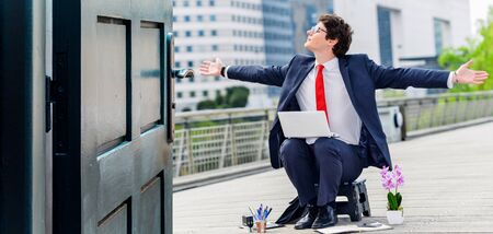 Opened door concept with humorous portrait of a businessman sitting on a stool with his arms wide open, with no desk outside in a business districtの写真素材