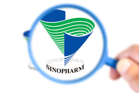 Benon, France - November 20, 2020: Sinopharm research laboratory logotype enlarged with a magnifying glass.This laboratory has developed a vaccine against the covid-19 virusのeditorial素材