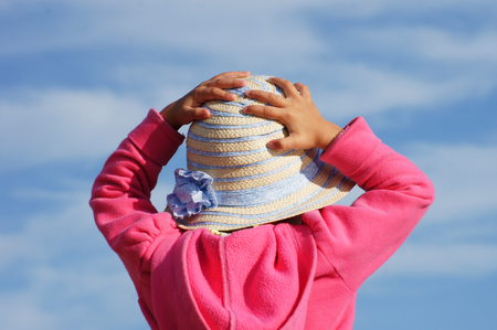Pink-dressed toddler is trying to catch her little straw hat in windy environment.の写真素材