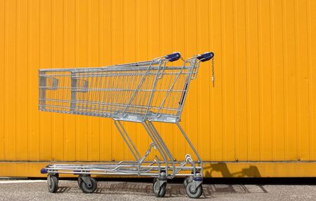 Two empty shopping carts in front of a yellow wallの写真素材
