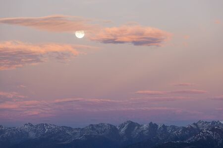 Sunset over the mountain peaks with full moonの写真素材