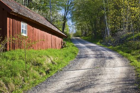 Uphill country road and a red barn in springのeditorial素材