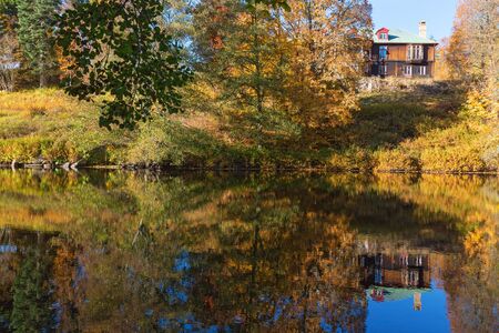 Autumn forest with a house on a hill reflecting in waterの写真素材