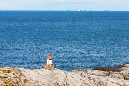 Small lighthouse on the rocky coast and ships at seaの写真素材