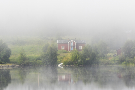 Red idyllic old cottage on a beach in fogの写真素材
