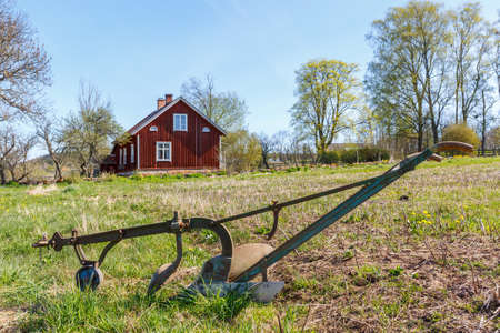 Old horse drawn plow the field with a red house in the backgroundのeditorial素材