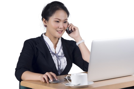 Portrait of business woman speaking on mobile phone while using laptop in office, Isolated white background. Model is Asian woman.  の写真素材