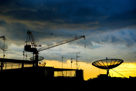 Silhouette of crane and satellite dish with dark rainy clouds on backgroundの写真素材