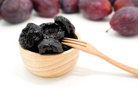 Delicious prunes in wooden bowl and fresh plums on backgroundの写真素材