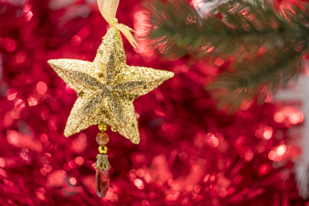Christmas star ornament hang on Christmas tree branch with red bokeh backgroundの写真素材