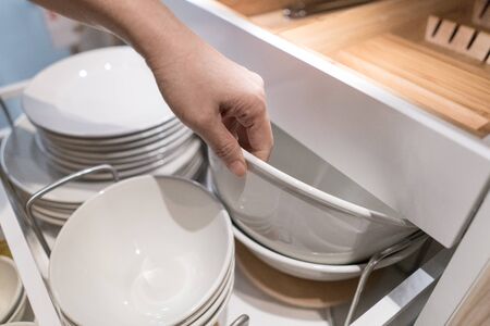 A hand is picking up a big white bowl out of drawer storage inside the modern kitchen cabinet, have separate and store proportionatelyの写真素材
