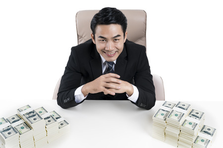 A young businessman smiling and the pile large amounts of money on desk, on white background, concept of business, financial and money laudering.の写真素材