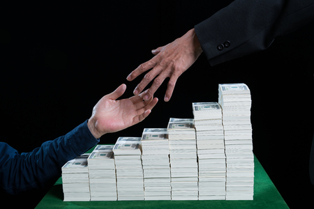 Two businessman outstretched hand going to shake against the stack of dollars placed on green table, black background in the casino business conceptの写真素材