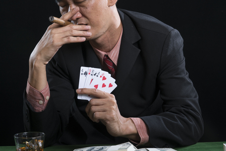 Close up the gambler is smoking for stress relief when he defeat in poker game, and holding show the lost point on black background with casino conceptの写真素材