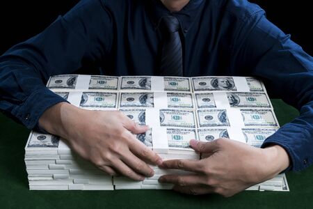 The businessman or rich man hugging the bundles stack of dollars on green table for the protection, on black background, financial business conceptの写真素材