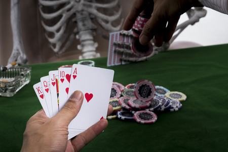 The hand of gamlber is putting chips into stacks of bets and show chance of winning blackjack gam, opponent is human skeleton and a pile of chips on the table at casinoの写真素材