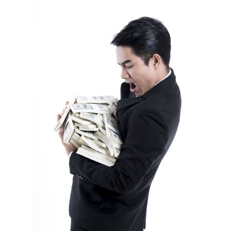 A side view of the young businessman carrying a large pile of money in his arms with excited expression on white backgroundの写真素材