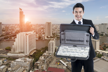 The Young businessman smiling and show the briefcase full of dollars standing on cityscape background, concept success business and financial
の写真素材