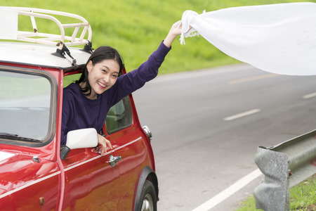 The young traveler out the window red car in holiday trip, cheerful and happy with the waving white cloth in hand, concept lifestyle and travelの写真素材