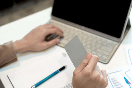 Selective focus at credit card in female hand and blurry background with laptop on table, copy space with Shopping Online conceptの写真素材