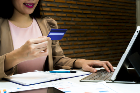 close up businesswoman hand holding credit card for buying online with a laptop and paying with a card, brick wall background, copy space with ecommerce technology conceptの写真素材