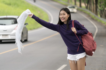 Asian young backpacker woman is smiling and waving white scraf in hand at along the way, concept lifestyle and travelの写真素材