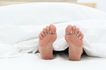 Close up human feet under white bed sheet with copy spaceの写真素材