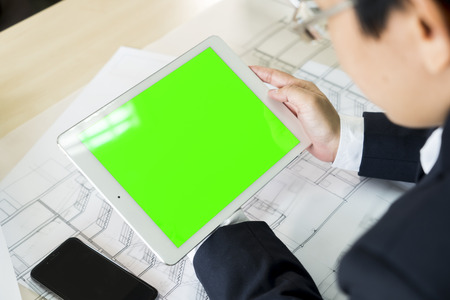 Close up and mock up green screen display on white tablet in businessman, smartphone and construction plan on wooden table.の写真素材